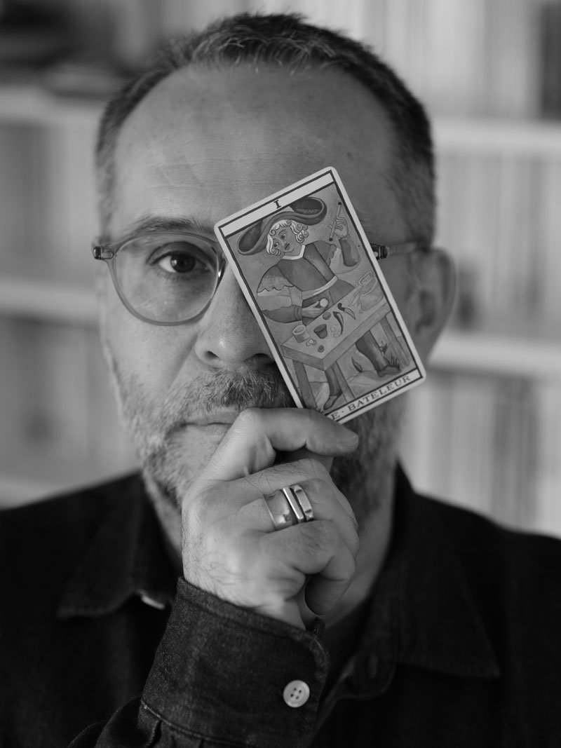 Nicolas Derouet, casting director, black-and-white portrait holding a tarot card.